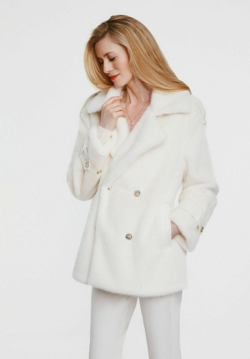Biały dwurzędowy płaszcz wykonany z miękkiego materiału, z wyłogowym kołnierzem, złotymi guzikami i kieszeniami po bokach.