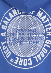 Blue hoodie featuring a large white graphic design with text and a globe pattern on the front. Material appears soft and textured.