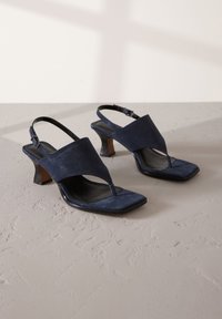 Sandales slingback en daim bleu marine avec un bout carré, un entre-doigt et un talon effilé. Présentent une texture lisse et un design minimaliste.