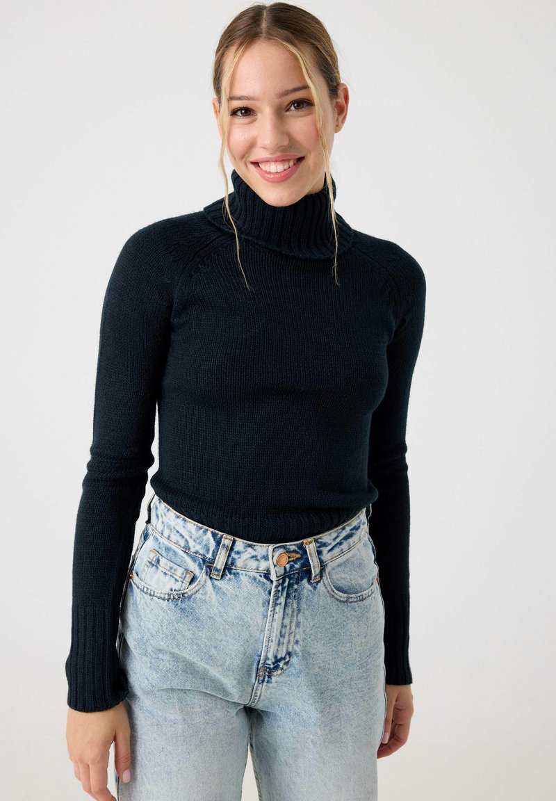 Suéter de cuello alto de navy con una textura acanalada, combinado con jeans de mezclilla claros de talle alto que presentan un patrón desgastado y bolsillos estándar.
