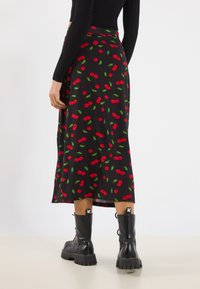 Schwarzer Midirock mit rotem Kirschmuster und grünen Blättern. Weicher Stoff, schwingendes Design und glatte Textur. Kombiniert mit schwarzen Combat Boots.