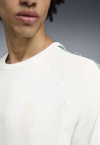 Weißes Baumwoll-Sweatshirt mit einem dezenten geprägten Logo, Raglanärmeln und grünen gemusterten Akzenten an den Schultern.
