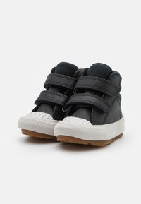 Zapatos de caña alta negros con parte superior de cuero sintético y tejido, doble tira de Velcro, puntera de goma blanca y suela texturizada blanca y de goma.