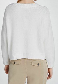 Vit stickad tröja med ribbad halsringning och nederkant, med en kort design. Kombinerad med beige byxor som har bakfickor och knappar.