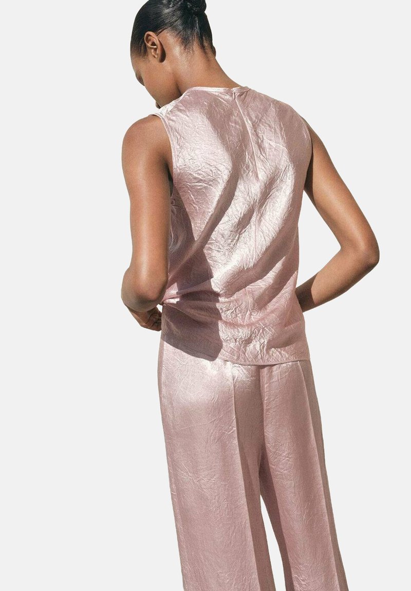 Top in tessuto rosa sgualcito con scollatura a barchetta, abbinato a pantaloni a gamba larga coordinati. Texture liscia con una leggera lucentezza.