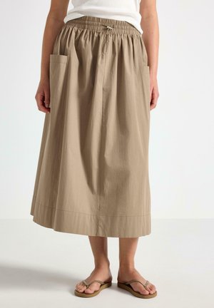 Beige midi-nederdel med elastisk talje og store forlommer, båret med hvid top og beige flip-flops på stående person.