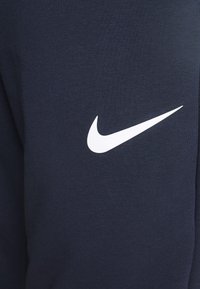 Námořnická modrá atleická tkanina s výrazným bílým logem Nike swoosh. Textura vypadá hladce s ribbovaným vzorem.