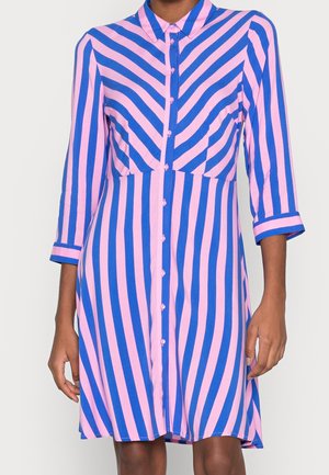 Woman wearing a button-up dress with blue and pink vertical and diagonal stripes and three-quarter length sleeves.