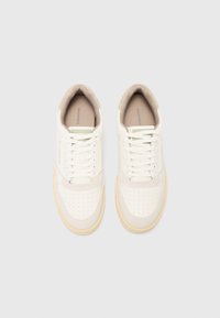 White and beige sneakers with a suede accent, perforated toe section, textured sole, and flat laces. Features branding on the tongue.