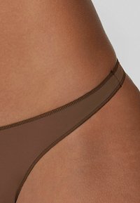 Brązowy dół bikini o gładkiej, matowej fakturze, z cienkim paskiem w talii i minimalistycznym designem. Szwy są subtelne i w tonacji materiału.