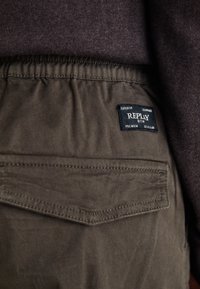 Khaki katoenen cargobroek met elastische tailleband, met een achterzak en een zwart label met witte tekst "REPLY PREMIUM SELECTION."