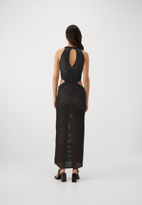 Robe maxi en tricot noir avec un dos en trou de serrure, des découpes latérales et une texture respirante. Associée à des sandales à talons carrés noires.