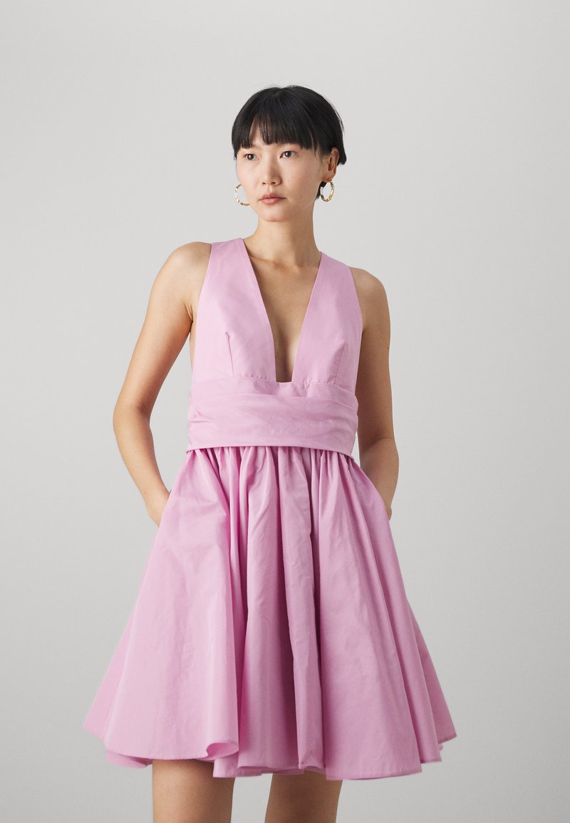 Robe sans manches rose avec un décolleté en V profond, jupe drapée et poches. Conçue en tissu lisse avec une silhouette structurée.
