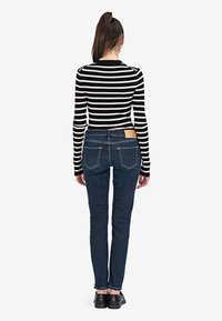 Mustavalkoraidallinen pitkähiha toppi, yhdistettynä tummansinisiin kapeisiin farkkuihin, joissa on takataskut ja vaaleanruskea etiketti vyötäröllä.