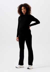 Haut noir à manches longues associé à un pantalon noir, fabriqué en tissu extensible, silhouette ajustée, porté avec des baskets blanches et grises.