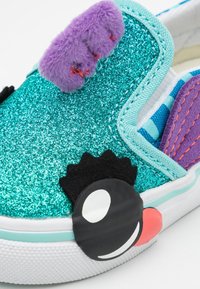 Kimallellinen turkoosi lenkkari purppuravilla elementeillä, musta-valkoinen silmädetalji ja raidallinen vuori. Varustettu litteällä valkoisella pohjalla ja kumisella varvaskärjellä.