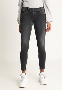 Schwarze Skinny Jeans aus dunklem Denim mit einem verwaschenen Look, fünf Taschen und leicht fransigen Säumen. Kombiniert mit weißen Sneakers.