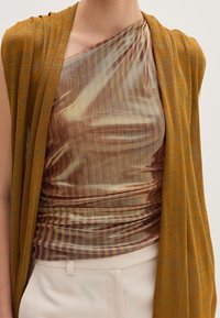 Brązowy i złoty lekki sweter o luźnym kroju, nałożony na wielokolorową, przezroczystą bluzkę z delikatnymi poziomymi paskami oraz marszczeniem w talii.