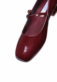 Scarpe Mary Jane in vernice bordeaux con punta arrotondata, una sottile cinturino e un tacco a blocco basso, caratterizzate da una superficie liscia e lucida.