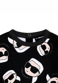 Felpa nera con collo rotondo, caratterizzata da volti ripetitivi in stile cartone animato, capelli bianchi e occhiali da sole. Tessuto morbido con una texture liscia.