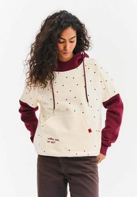 Kremowa bluza z pulowerem z bordowymi rękawami. Ma wzór w kropki, kieszeń z przodu oraz napis "kawa, herbata, czy ja?"