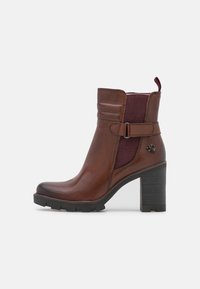 Bottine en cuir brun avec un panneau élastique texturé bordeaux, accent de boucle et un large talon noir, dotée d'une semelle crantée pour une meilleure adhérence.