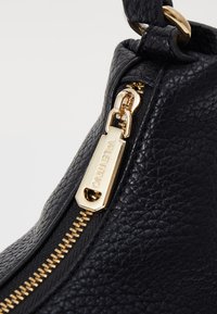 Black textured leather bag featuring a gold zipper with a gold pull tag engraved with "Valentino." Simple and sleek design detail.