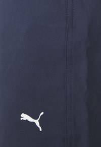 Navy blue jogger pants made of textured fabric, featuring a prominent white Puma logo and visible stitching along the side seam.
