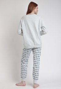 Sudadera gris claro con puños acanalados, combinada con pantalones gris claro que presentan patrones de corazones en azul marino y cinturilla elástica. Modelo descalzo mostrado.