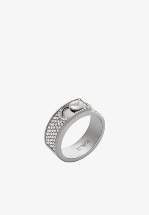 Anillo de plata con una banda lisa, decorado con una fila de cristales transparentes y un pequeño emblema circular en el lateral.