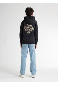 Felpa nera con grafica di un albero digitale e testo "PETROL IND" sulla schiena. Abbinata a jeans blu chiaro e sneaker bianche.