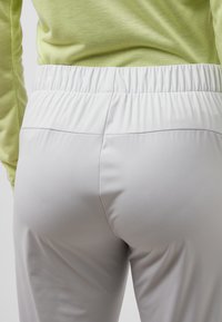 Lichtgrijze, elastische broek met een elastische tailleband, met een gladde textuur en minimale naden, gecombineerd met een limoengroen t-shirt met lange mouwen.