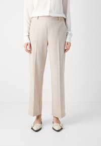 Beige Leinenhosen mit glatter Textur, geradem Bein und subtiler Ausführung. Kombiniert mit einer weißen Bluse und cremefarbenen Mokassins.