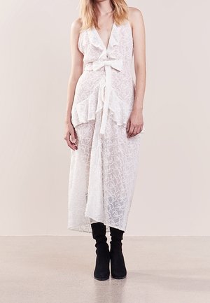 Robe blanche en dentelle avec un col en V, des bords froncés et un lien à l'avant. Présente un ourlet asymétrique et un design en couches. Portée avec des bottes noires.