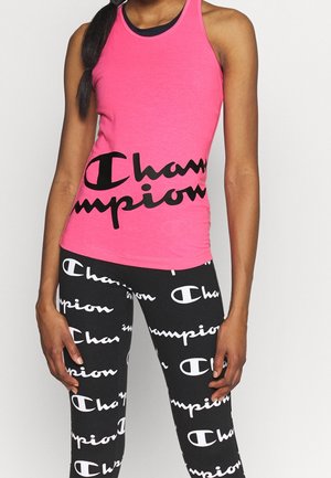 Roze sporttop met zwart "Champion" logo, gecombineerd met zwarte leggings met een herhaalpatroon van witte logo's.
