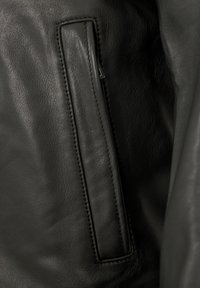 Nahaufnahme einer schwarzen Lederjackentasche mit sichtbarem Reißverschluss und detaillierter Naht auf glattem, strukturiertem Leder.