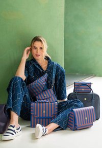 Multi-colored striped bags in blue and orange, made of smooth material, arranged by a person in blue patterned outfit and white shoes.