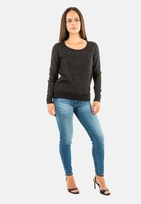 Pull en maille métallique noir avec un col rond, associé à un jean skinny bleu clair et des talons hauts ouverts noirs. Design simple.