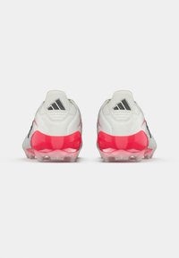 Λευκά αθλητικά παπούτσια με υφή στο επάνω μέρος, μαύρες λεπτομέρειες και ροζ σόλα με διαβάθμιση. Διαθέτουν τρεις μαύρες ρίγες κοντά στη φτέρνα.