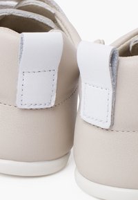 Scarpe in pelle beige chiaro con linguette posteriori in tessuto bianco, caratterizzate da dettagli cuciti e una superficie liscia. Design arrotondato e suole in gomma bianca.