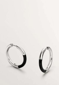 Pendientes de aro de plata con un diseño elegante, acabado brillante y un acento negro en un lado. Textura suave, forma circular.