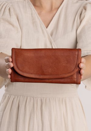 Portefeuille en cuir marron avec un rabat, des détails de couture visibles, une texture lisse et une forme rectangulaire, tenu dans des mains.