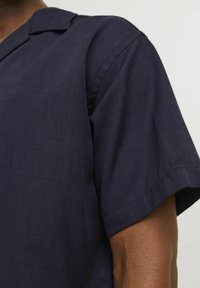 Navy short-sleeve shirt with a notched collar, featuring a textured fabric and clean stitching along the sleeves.