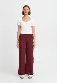 Vit kortärmad topp med fyrkantig halsringning, ihop med bordeaux färgade vida byxor med hög midja och sidofickor. Grå sneakers.