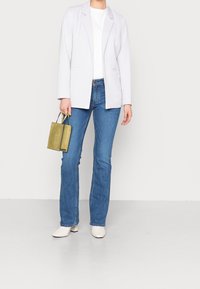 Blazer de color púrpura claro sobre una camiseta blanca, combinado con pantalones vaqueros azules y botines blancos. Sosteniendo un pequeño bolso texturizado en color verde oliva.