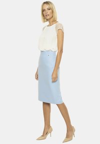 Jasnoniebieska spódnica ołówkowa o gładkiej fakturze, połączona z białą bluzką z przezroczystymi rękawami w groszki. Całość dopełniają cieliste szpilki.
