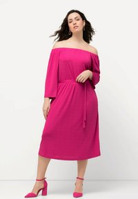 Vaaleanpunainen olkapäät paljastava mekko, jossa on vyötärösolmu, kolmen neljänneksen hihat ja lentävä siluetti. Yhdistetty samaan sävyyn vaaleanpunaisiin korkokenkiin.