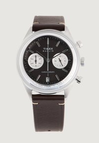 Timex Marlin kronograf sat ima okruglo kućište od nehrđajućeg čelika, crni brojčanik sa srebrnim podbrojčanicima i smešani kožni remen.
