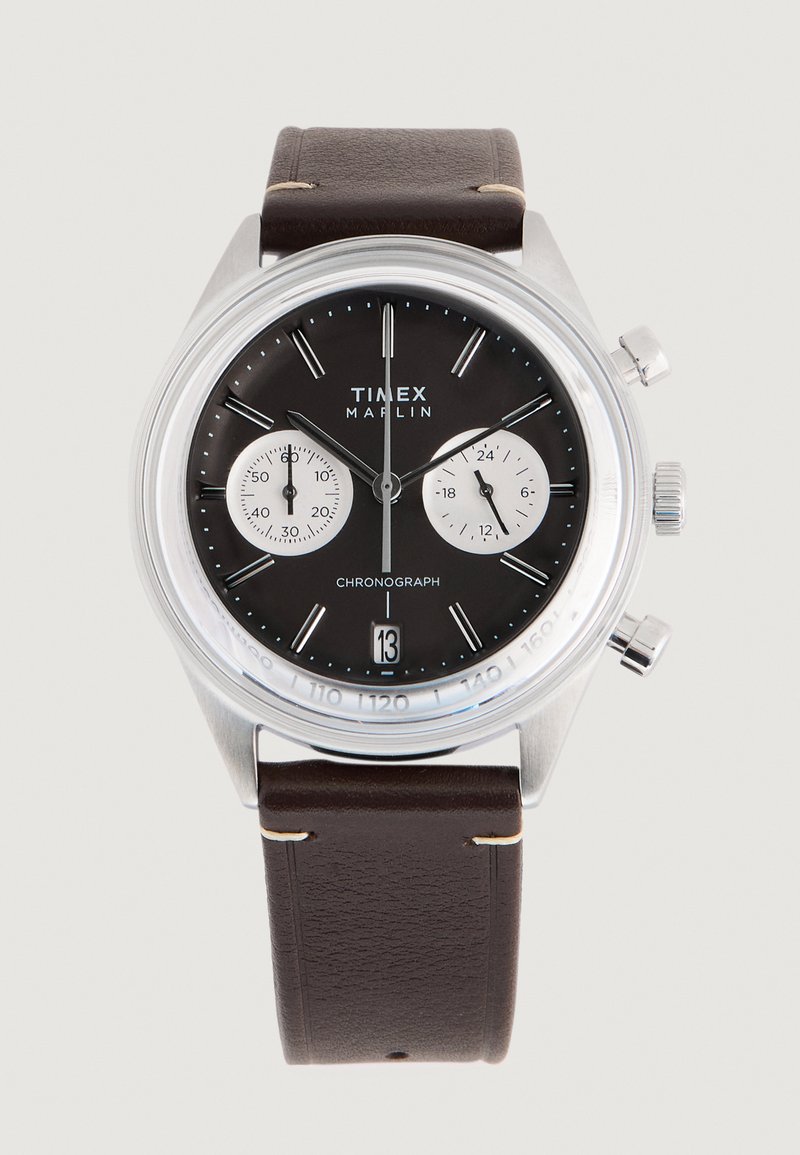 Timex Marlin kronograf sat ima okruglo kućište od nehrđajućeg čelika, crni brojčanik sa srebrnim podbrojčanicima i smešani kožni remen.