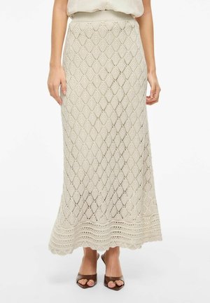 Jupe maxi en maille crochet beige avec motif en losanges et ourlet festonné, portée avec des talons ouverts marron.